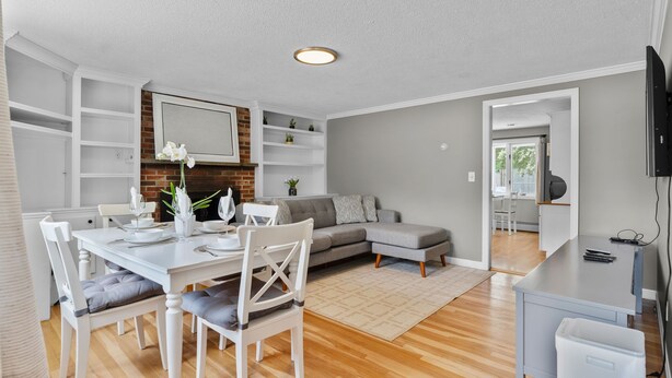 Una sala de estar moderna con comedor, un sofá gris, una mesa blanca con sillas y un televisor montado en la pared.