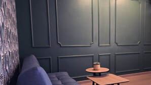 Ein modernes Interieur mit einer dunklen Wand, einem blauen Sofa und einem kleinen Holztisch mit einer Pflanze.