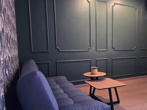 Ein modernes Interieur mit einer dunklen Wand, einem blauen Sofa und einem kleinen Holztisch mit einer Pflanze.