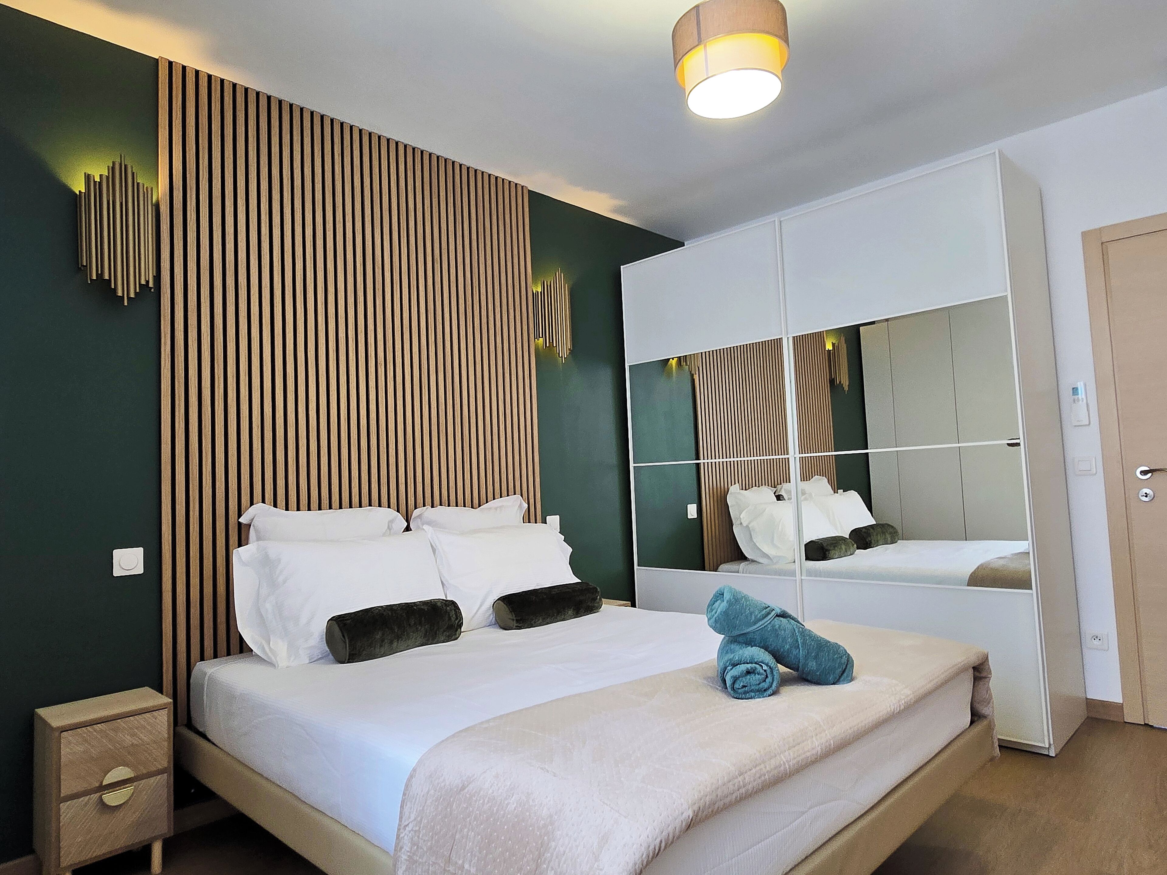 A modern bedroom with a bed, bedside tables, a mirror, and a wardrobe.