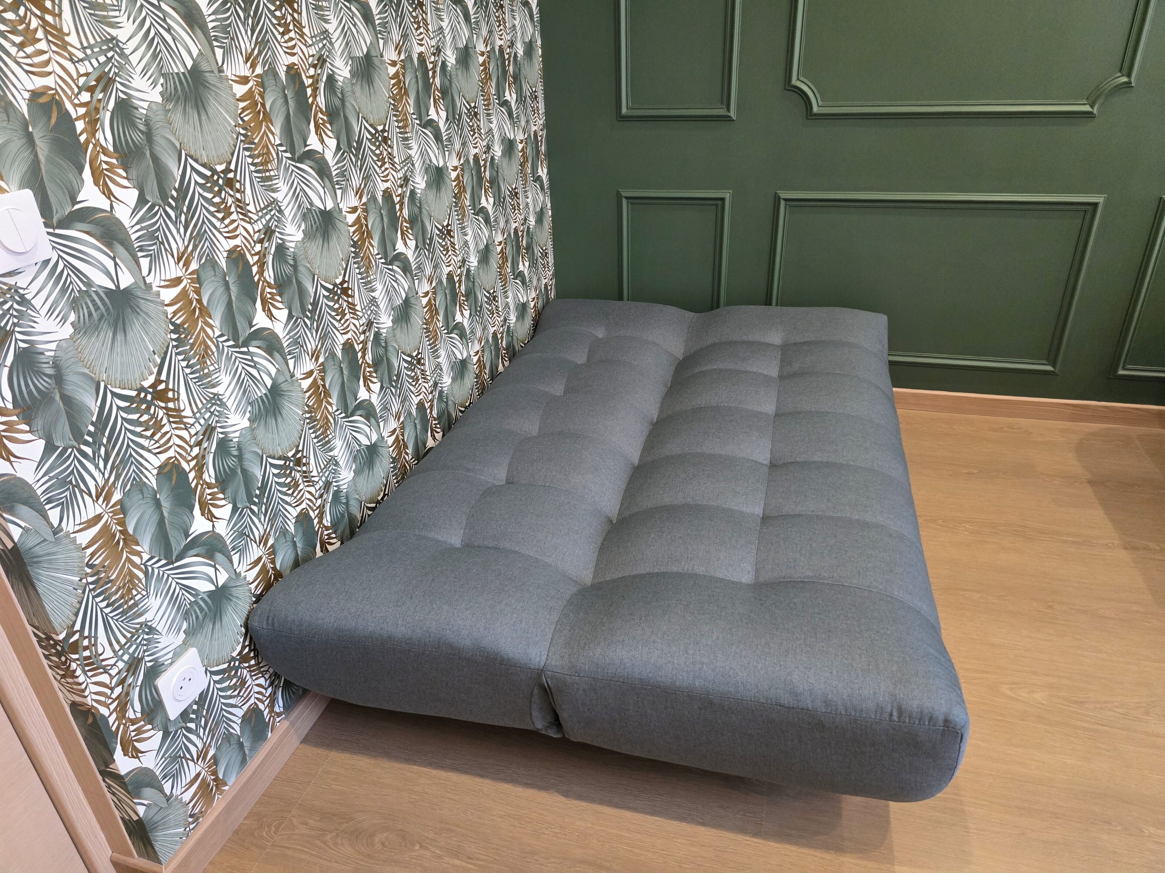 Ein Zimmer mit einer grau gepolsterten Bank, einem gemusterten Wandpapier und einer grünen Wand mit Paneelen.