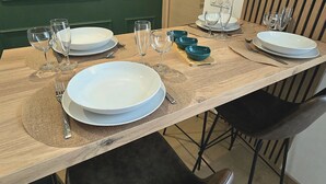 Ein Esstisch ist mit Tellern, Schüsseln, Gläsern und Besteck gedeckt, drumherum Stühle.