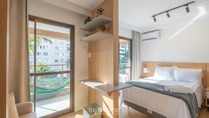 Ein modernes Hotelzimmer mit Bett, einem kleinen Tisch, einem Fenster mit Blick auf Gebäude und einer Hängematte draußen.