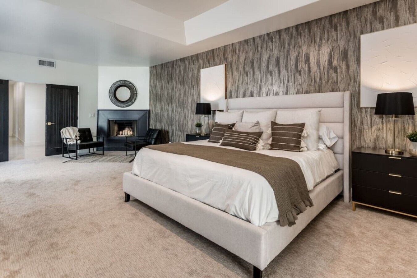 A spacious bedroom with a large bed, a fireplace, a seating area, and a modern wall design.
