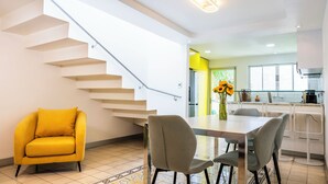 Eine moderne Küche mit weißen Schränken, ein Essbereich mit Tisch und Stühlen sowie eine Treppe mit einem gelben Sessel.