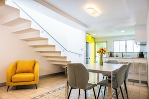 Eine moderne Küche mit weißen Schränken, ein Essbereich mit Tisch und Stühlen sowie eine Treppe mit einem gelben Sessel.