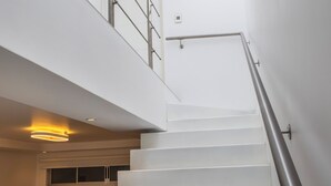Eine moderne Treppe mit Glasdach, Metallgeländer und einer Couch im unteren Zwischenpodest.