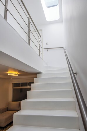 Eine moderne Treppe mit Glasdach, Metallgeländer und einer Couch im unteren Zwischenpodest.