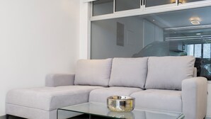 Ein modernes Wohnzimmer mit einem hellen Sofa, einem Glastisch und einem gemusterten Teppich.