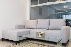 Ein modernes Wohnzimmer mit einem hellen Sofa, einem Glastisch und einem gemusterten Teppich.