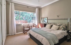 A bedroom with a bed, a chair, a dresser, a mirror, and a window with curtains. - Family sized house (Pretoria)
