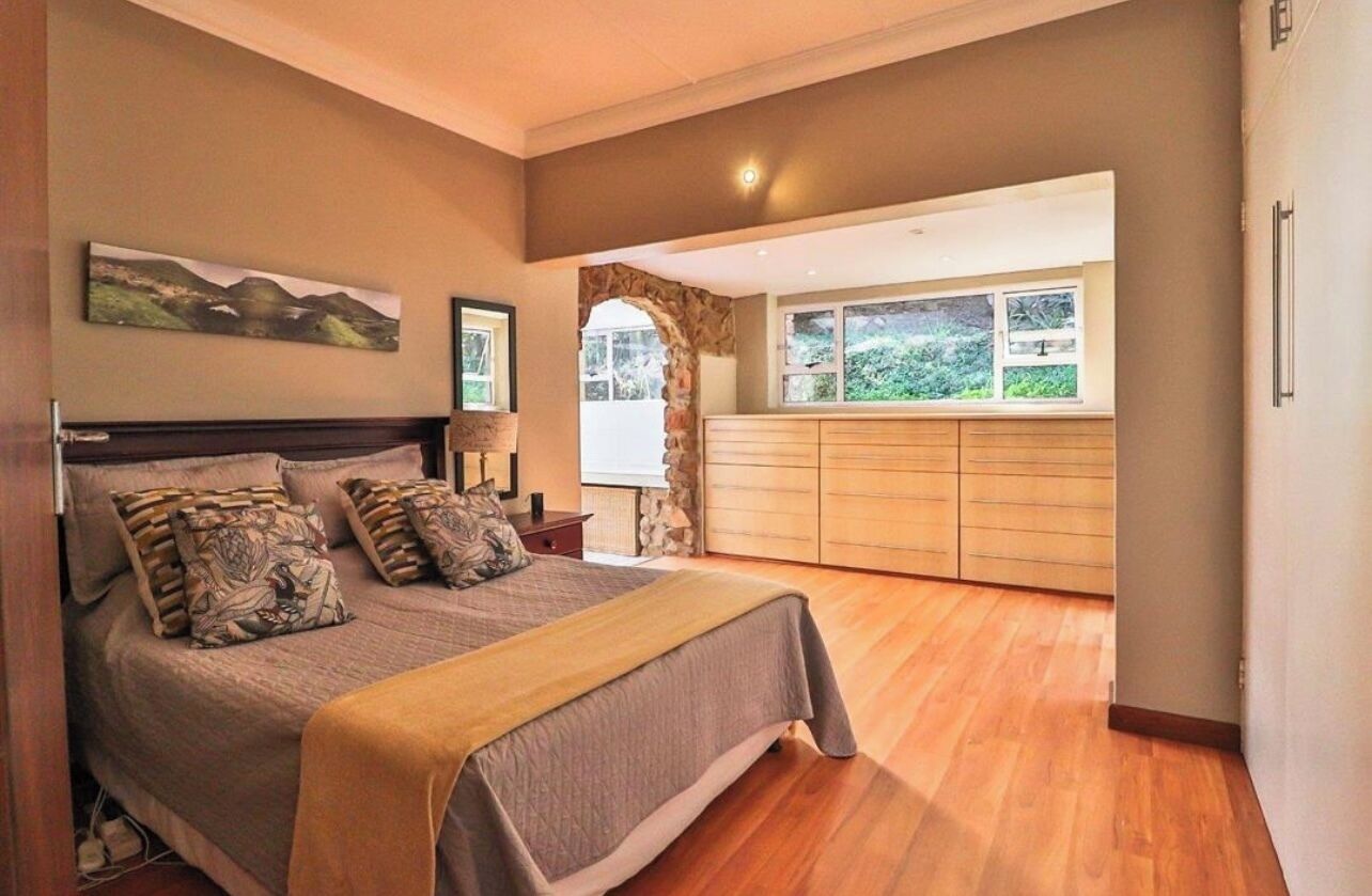 A bedroom with a bed, a dresser, a window, and a stone archway.