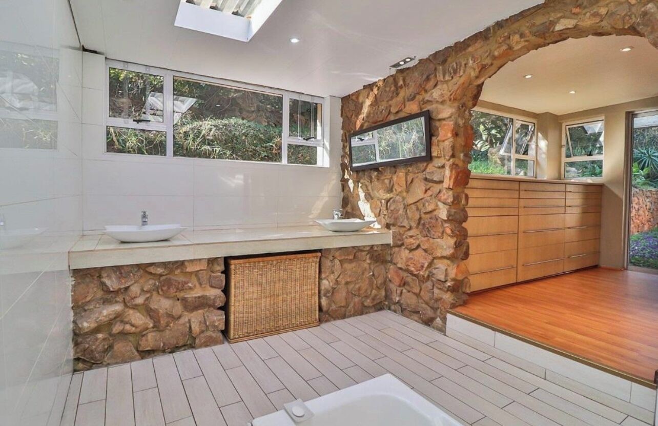 A modern bathroom with a stone wall, a large sink, a bathtub, and a wooden vanity.