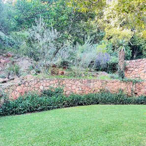 Un jardín ajardinado con muro de piedra, arbustos y árboles.