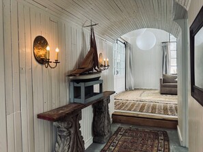 Una habitación con un banco de madera, un modelo de barco, un candelabro en la pared y una alfombra estampada.