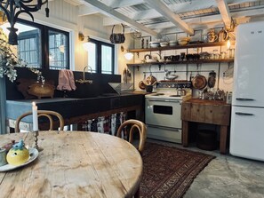 A kitchen with a wooden table, a stove, and various kitchen utensils.