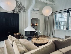 A cozy interior with a fireplace, a sofa, a round wooden table, and large windows.