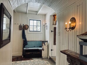 A rustic room with a wooden bench, a window, a wall-mounted light fixture, and a mirror.