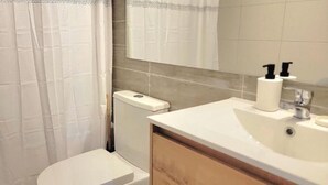 A bathroom with a toilet, a sink, a mirror, and a shower curtain. - RBK moderno Studio pasos de Club Hípico (Santiago)