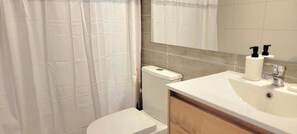 A bathroom with a toilet, a sink, a mirror, and a shower curtain. - RBK moderno Studio pasos de Club Hípico (Santiago)