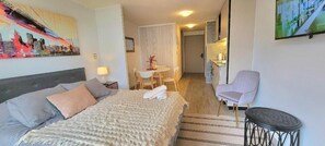 A hotel room with a bed, a small table with chairs, a TV, and a chair. - RBK moderno Studio pasos de Club Hípico (Santiago)