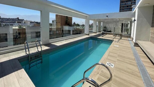 A rooftop pool with clear blue water, surrounded by a wooden deck and glass railings. - RBK moderno Studio pasos de Club Hípico (Santiago)