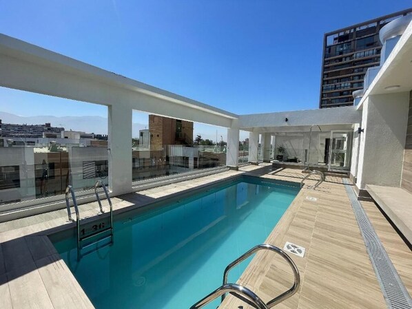 A rooftop pool with clear blue water, surrounded by a wooden deck and glass railings. - RBK moderno Studio pasos de Club Hípico (Santiago)