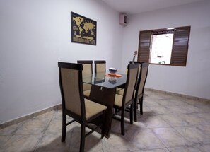 Un comedor con una mesa de vidrio y cuatro sillas, un mapa del mundo en la pared y una ventana con persianas.