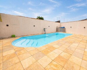 A rectangular swimming pool with a tiled deck, surrounded by a low wall with a small step leading to the pool. - Casa com Piscina e Churrasqueira Perto do Centro (Uberlandia)