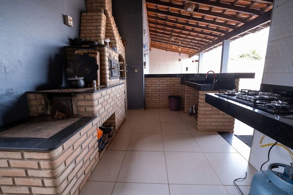 A kitchen with a brick oven, gas stove, tiled floor, and a wooden ceiling.