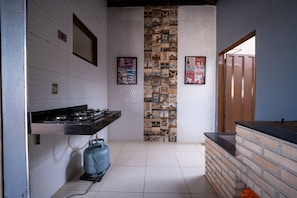 A kitchen with a gas stove, a blue gas cylinder, a brick accent wall, and a vertical collage of images.