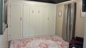 A room with a large white wardrobe, a patterned carpet, a red sofa, and a ceiling light.