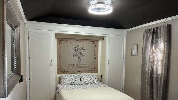 A bedroom with a bed, a wall-mounted artwork, a ceiling light, and a patterned rug.