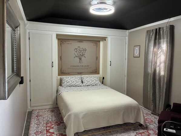 Un dormitorio con cama, una obra de arte en la pared, una lámpara de techo y una alfombra estampada.