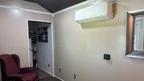 A hallway with a red chair, an air conditioning unit, a door with a picture, and a wall-mounted light switch.