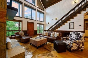 A spacious living room with leather sofas, a patterned ottoman, a cowhide rug, and a staircase leading to an upper level. - Pour Me - Luxury Cabin; Carter Mtn; Sleeps 12 (McCurtain County)