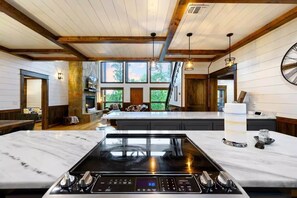 A kitchen with a large island, a stone fireplace, and a view of the outdoors. - Pour Me - Luxury Cabin; Carter Mtn; Sleeps 12 (McCurtain County)
