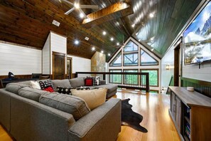 A spacious living area with a large sofa, wooden ceiling, and a view through large windows. - Pour Me - Luxury Cabin; Carter Mtn; Sleeps 12 (McCurtain County)