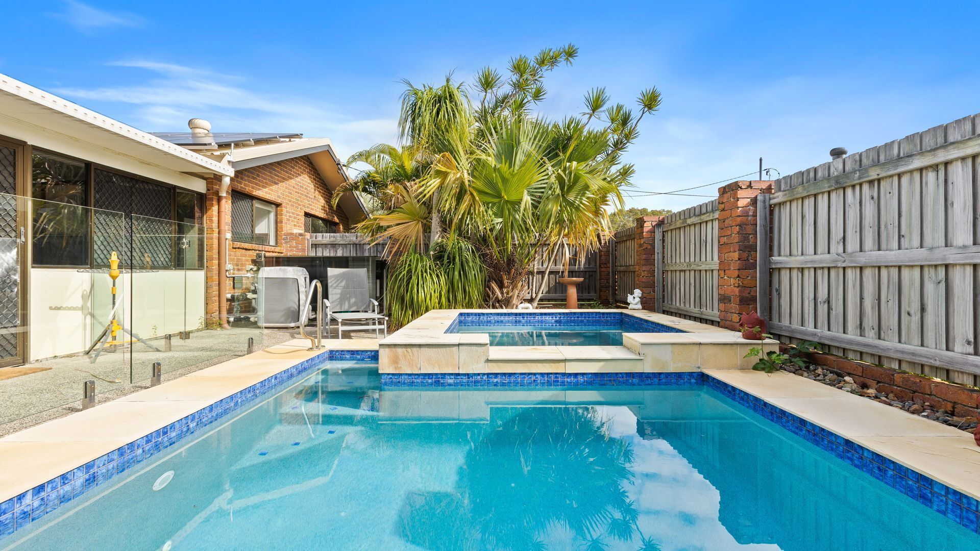 A swimming pool with a tiled edge, surrounded by a brick wall and a wooden fence.