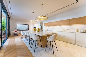 A modern kitchen with a large island, bar stools, pendant lights, and a view of the outdoors. - Villa Émeraude: A stunning villa located 150 meters from the beach. (Arcachon)