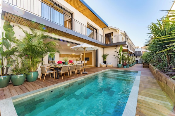 A modern building with a pool, outdoor seating, and potted plants.