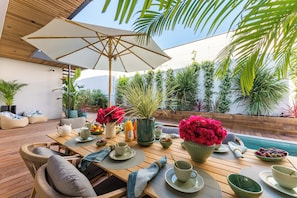 An outdoor dining area with a wooden table, chairs, a large umbrella, and various plants and flowers. - Villa Émeraude: A stunning villa located 150 meters from the beach. (Arcachon)