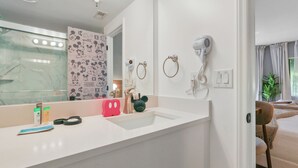 A bathroom with a white sink, a Mickey Mouse-themed mirror, a hairdryer, and a towel ring. - Studio near Universal, Epic & I-Drive (Orlando)