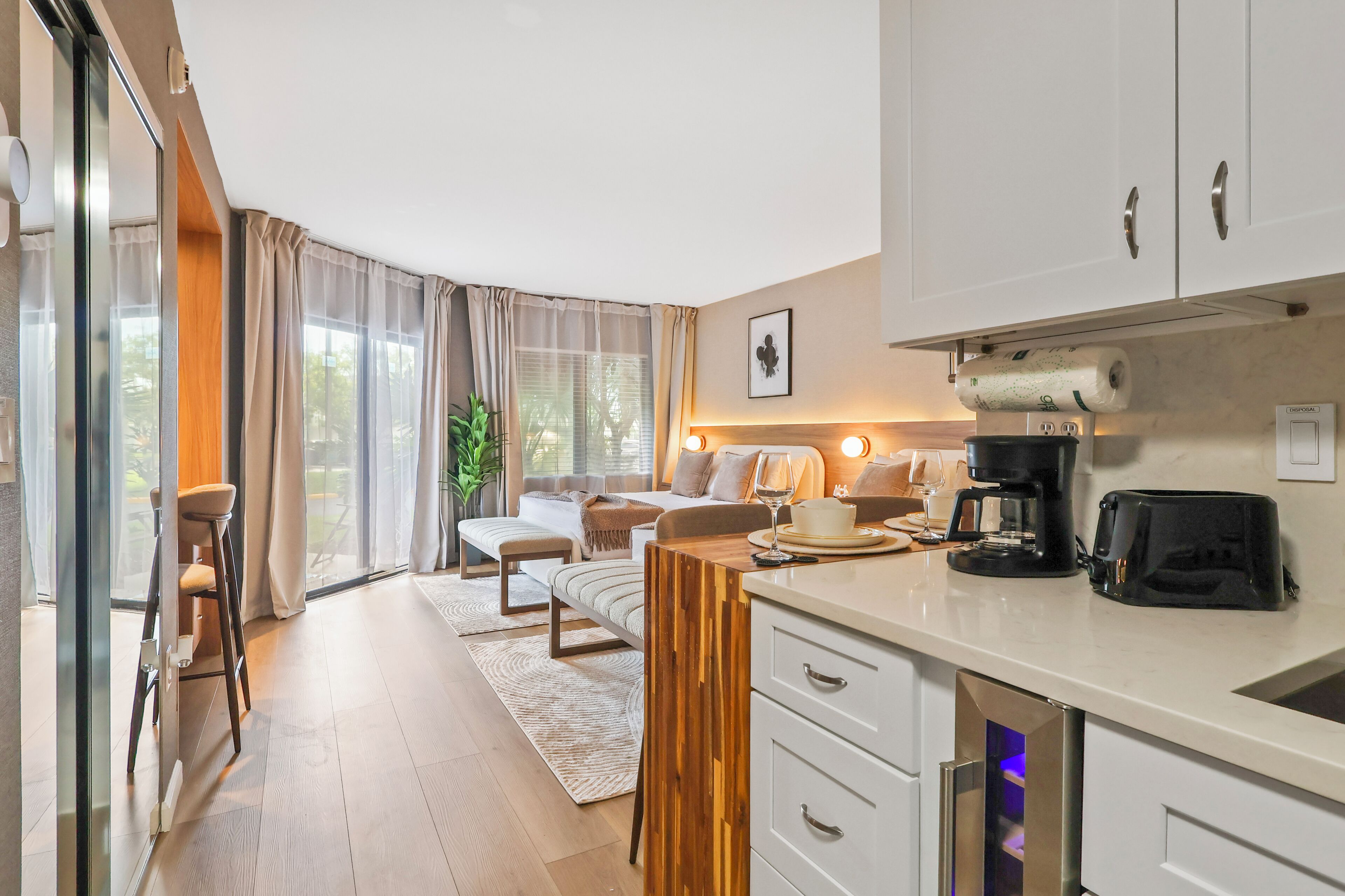 Eine moderne Küche mit integriertem Backofen, Kaffeemaschine und Toaster. Es gibt einen Essbereich mit Tisch und Stühlen sowie ein großes Fenster mit Vorhängen.