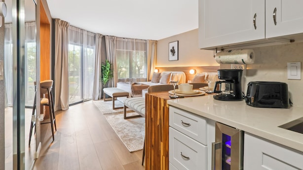 A modern kitchen with a built-in oven, a coffee maker, and a toaster. There is a dining area with a table and chairs, and a large window with curtains. - Studio near Universal, Epic & I-Drive (Orlando)