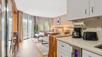Eine moderne Küche mit integriertem Backofen, Kaffeemaschine und Toaster. Es gibt einen Essbereich mit Tisch und Stühlen sowie ein großes Fenster mit Vorhängen.