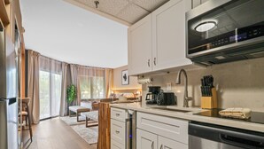 A modern kitchen with stainless steel appliances, a dining area with a wooden table and chairs, and a view of the outdoors through large windows. - Studio near Universal, Epic & I-Drive (Orlando)