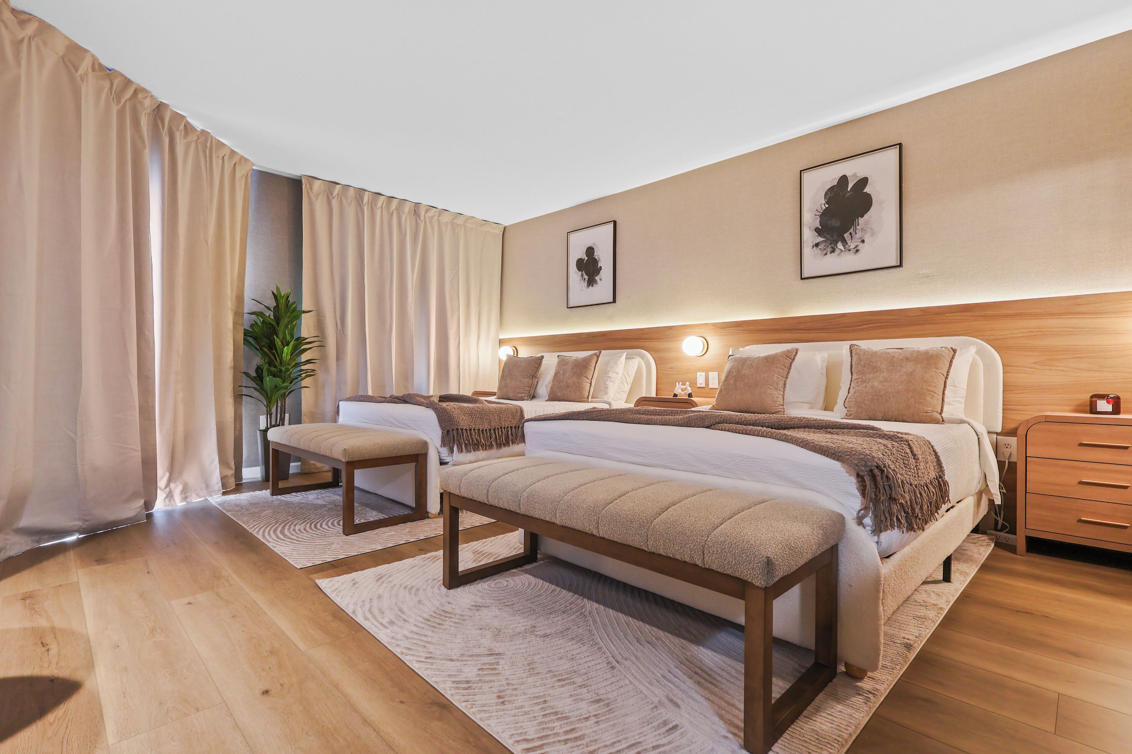 Ein modernes Hotelzimmer mit zwei Betten, einer Bank, einem Nachttisch und einer Topfpflanze.