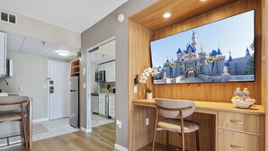 A modern kitchen with wooden cabinetry, a large flat-screen TV, and a dining area with bar stools. - Studio near Universal, Epic & I-Drive (Orlando)