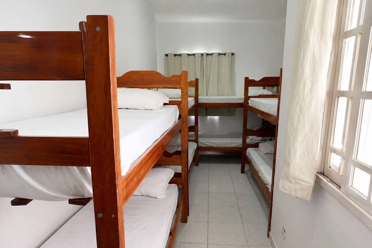 A room with bunk beds, a window with curtains, and a tiled floor.